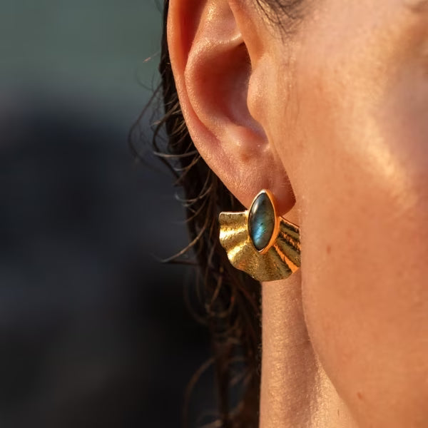 Nahaufnahme: Ein edler Alun-Ohrring von ILUH in Fächerform, vergoldet und besetzt mit einem schimmernden blaugrünen Labradorit Edelstein. Das hochwertige, in Bali handgefertigte Schmuckstück aus recyceltem 925 Sterling Silber verbindet organische Formen mit spiritueller Eleganz und dem typischen Beach-Vibe der Marke.
