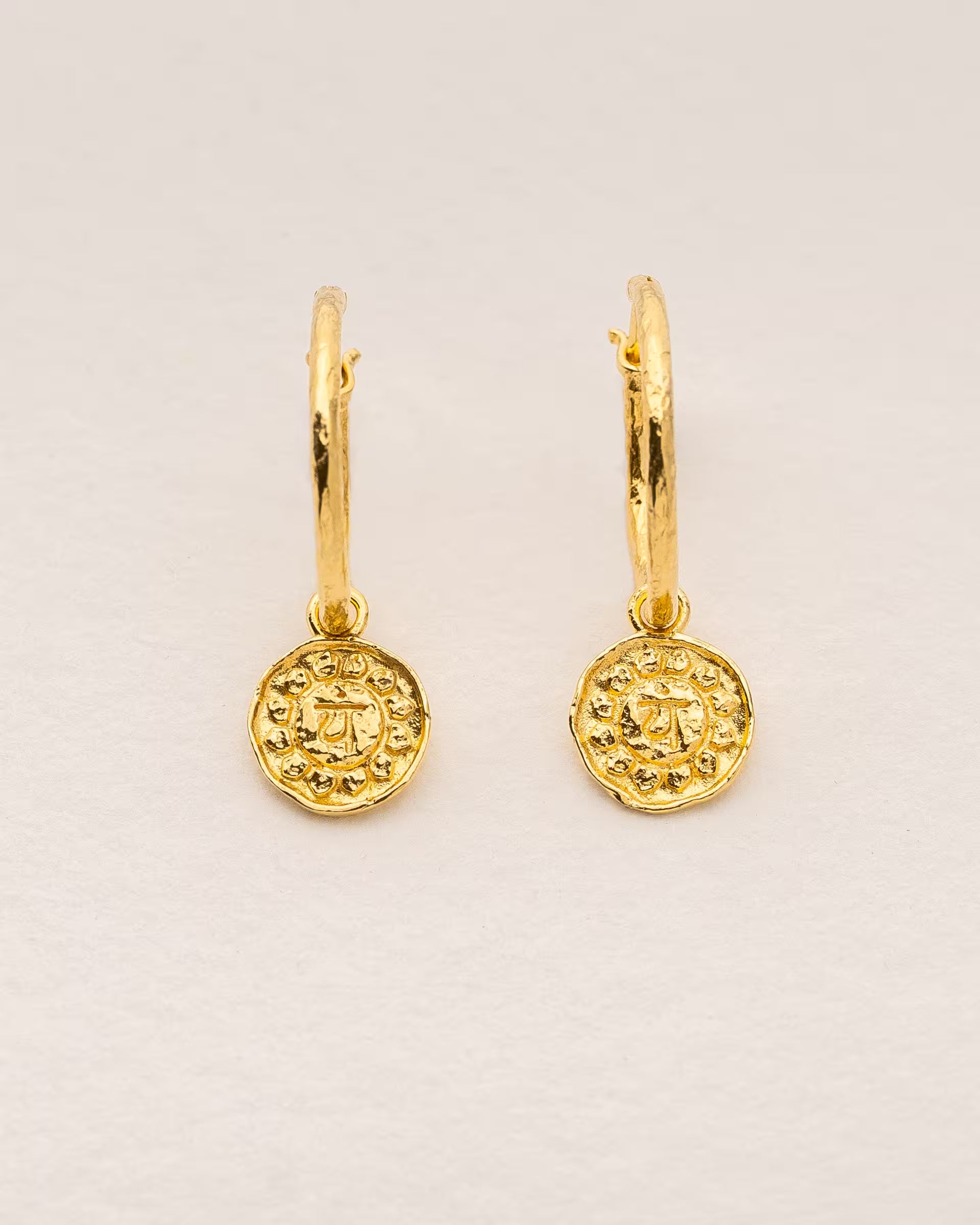 #Motiv_Anahata CHAKRA ANAHATA OHRRINGE GOLD Produktbild – Diese handgefertigten Ohrringe von ILUH aus Bali im minimalistischen Boho-Stil bestehen aus strukturierten Creolen mit einem Anhänger des originalen Sanskrit-Zeichens für das Anahata-Herzchakra; eingebettet in kunstvolle Lotusblütenblätter dienen sie als kraftvolles Symbol zur Stärkung deines Energiezentrums.