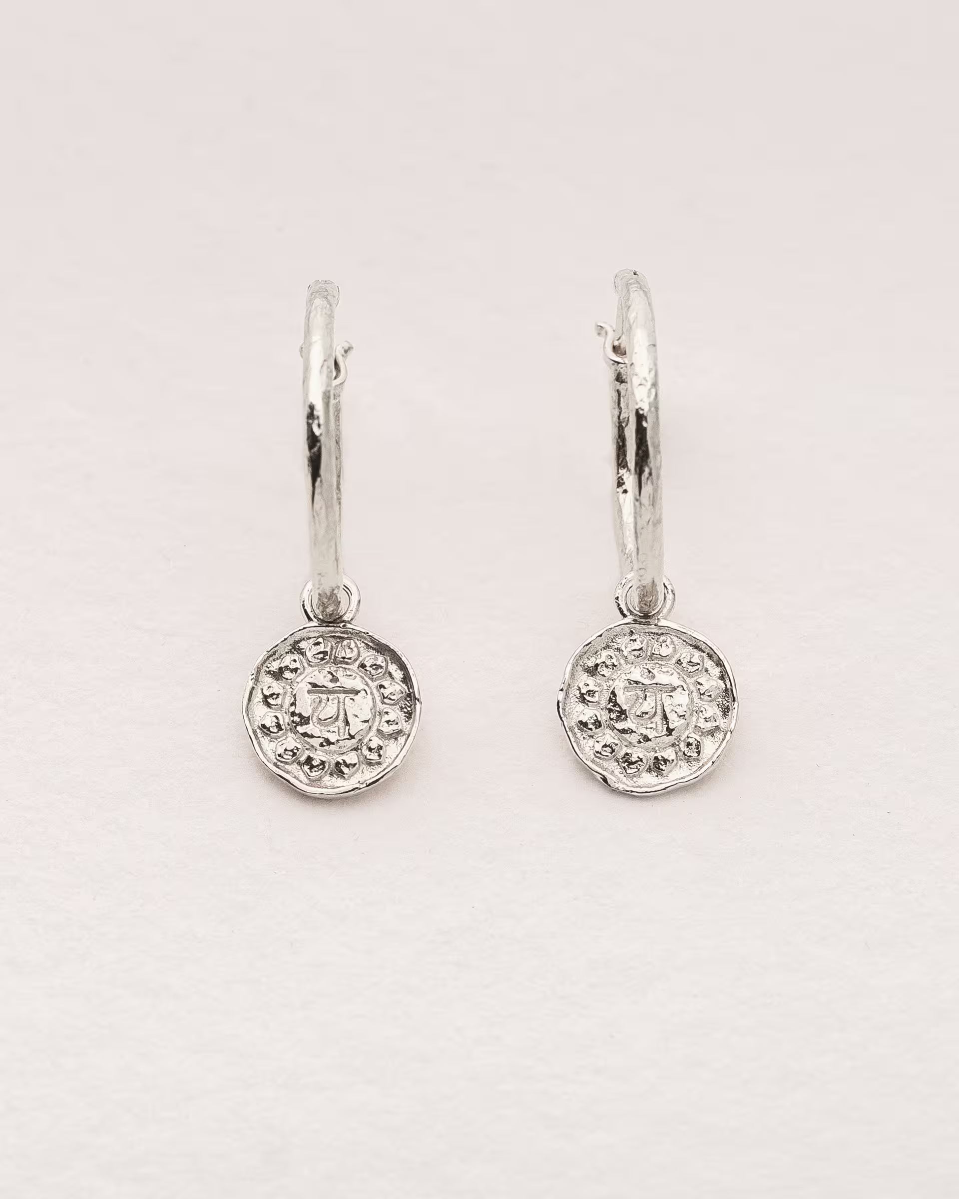 #Motiv_Anahata CHAKRA ANAHATA OHRRINGE SILBER Produktbild – Diese handgefertigten Ohrringe von ILUH aus Bali im minimalistischen Stil bestehen aus strukturierten Creolen mit einem Anhänger des originalen Sanskrit-Zeichens für das Anahata-Herzchakra; eingebettet in kunstvolle Lotusblütenblätter dienen sie als kraftvolles Symbol zur Stärkung deines Energiezentrums.