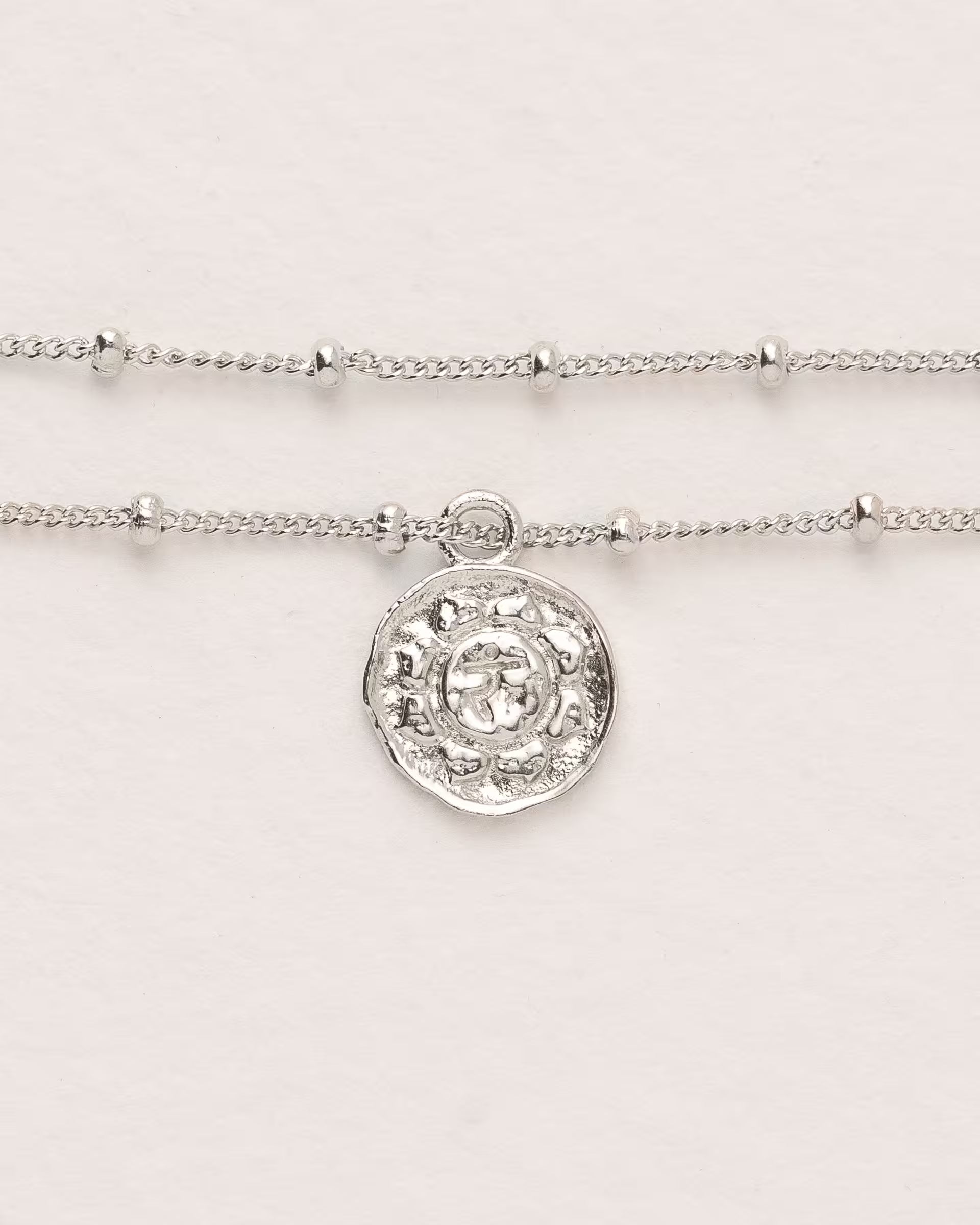 #Motiv_Manipura CHAKRA MANIPURA ARMBAND SILBER, silbernes Armband von ILUH, handgefertigt auf Bali – Spirituelles Produktfoto im minimalistischen Boho-Look von einem feinen Satellitenarmband aus 925er Silber mit einem runden Münzanhänger, der das originale Sanskrit-Zeichen für das Manipura-Solarplexuschakra, eingebettet in kunstvolle Lotusblütenblätter zur Stärkung des Energiezentrums, zeigt.