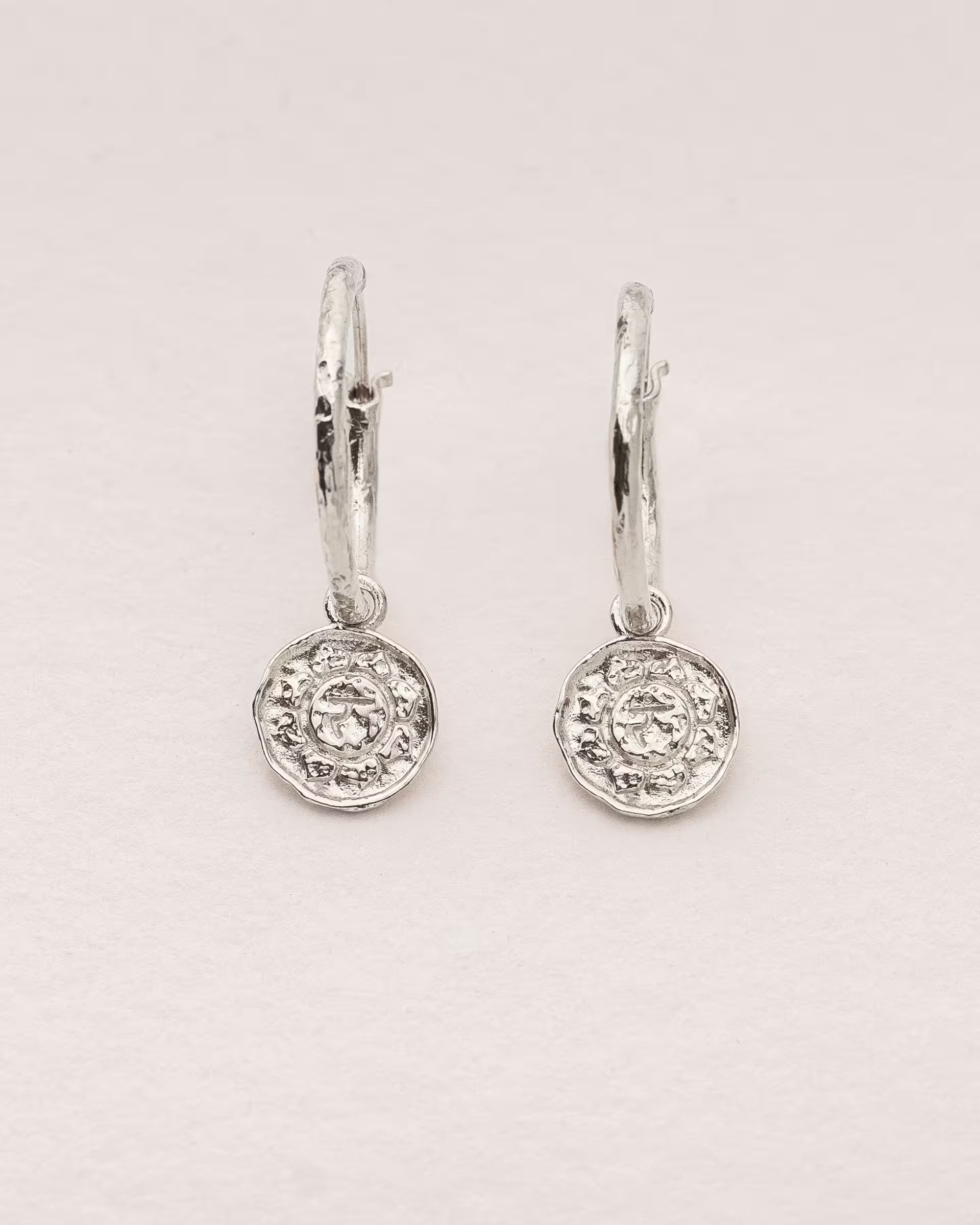 #Motiv_Manipura CHAKRA MANIPURA OHRRINGE SILBER Produktbild – Diese handgefertigten Ohrringe von ILUH aus Bali im minimalistischen Boho-Stil bestehen aus strukturierten Creolen mit einem Anhänger des originalen Sanskrit-Zeichens für das Manipura-Solarplexuschakra; eingebettet in kunstvolle Lotusblütenblätter dienen sie als kraftvolles Symbol zur Stärkung deines Energiezentrums.