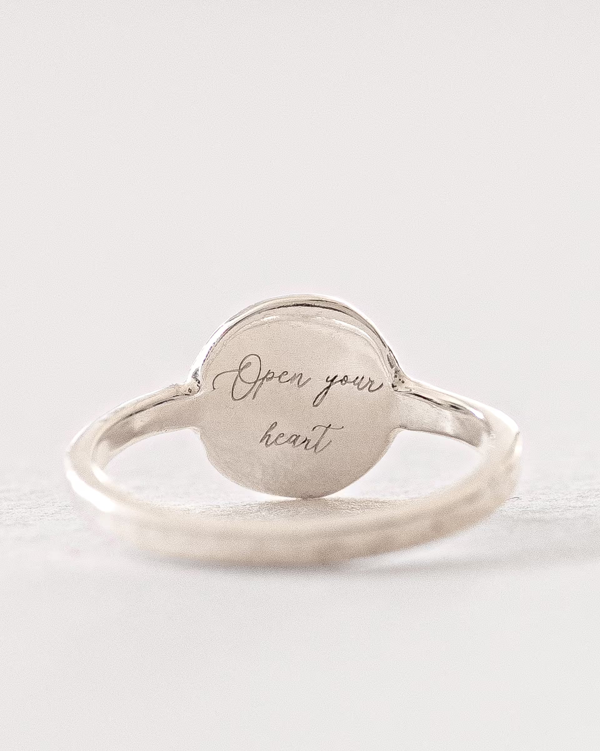 Filigraner ILUH Chakra-Ring aus 925er Sterlingsilber mit einer handgefertigten Gravur ‚Open your heart‘; eine Repräsentation des Anahata-Chakra (Herzchakra), das für Liebe und innere Balance steht. Präsentiert in minimalistischer Ästhetik auf hellem Untergrund, ideal für modernen, achtsamen Schmuck.