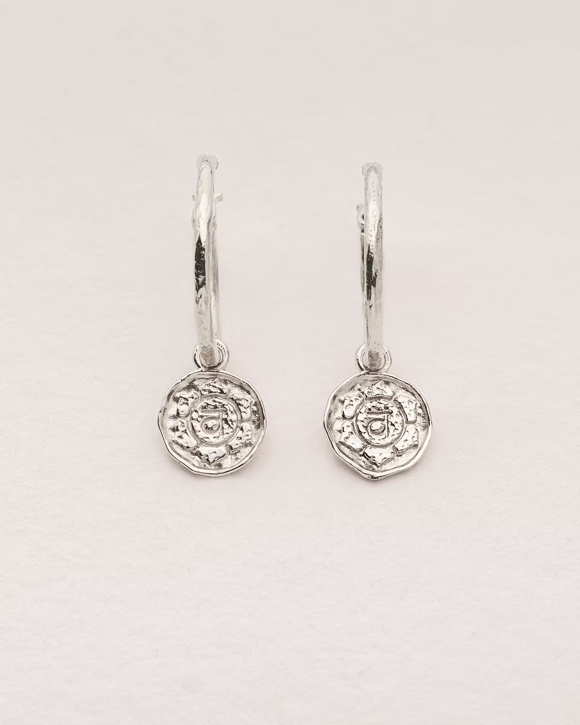 #Motiv_Svadhisthana CHAKRA SVADHISTHANA OHRRINGE SILBER Produktbild – Diese handgefertigten Ohrringe von ILUH aus Bali im minimalistischen Boho-Stil bestehen aus strukturierten Creolen mit einem runden Anhänger, der das originale Sanskrit-Zeichen für das Svadhisthana-Sakralchakra zeigt; eingebettet in kunstvolle Lotusblütenblätter dienen sie als kraftvolles Symbol zur Stärkung deines Energiezentrums.