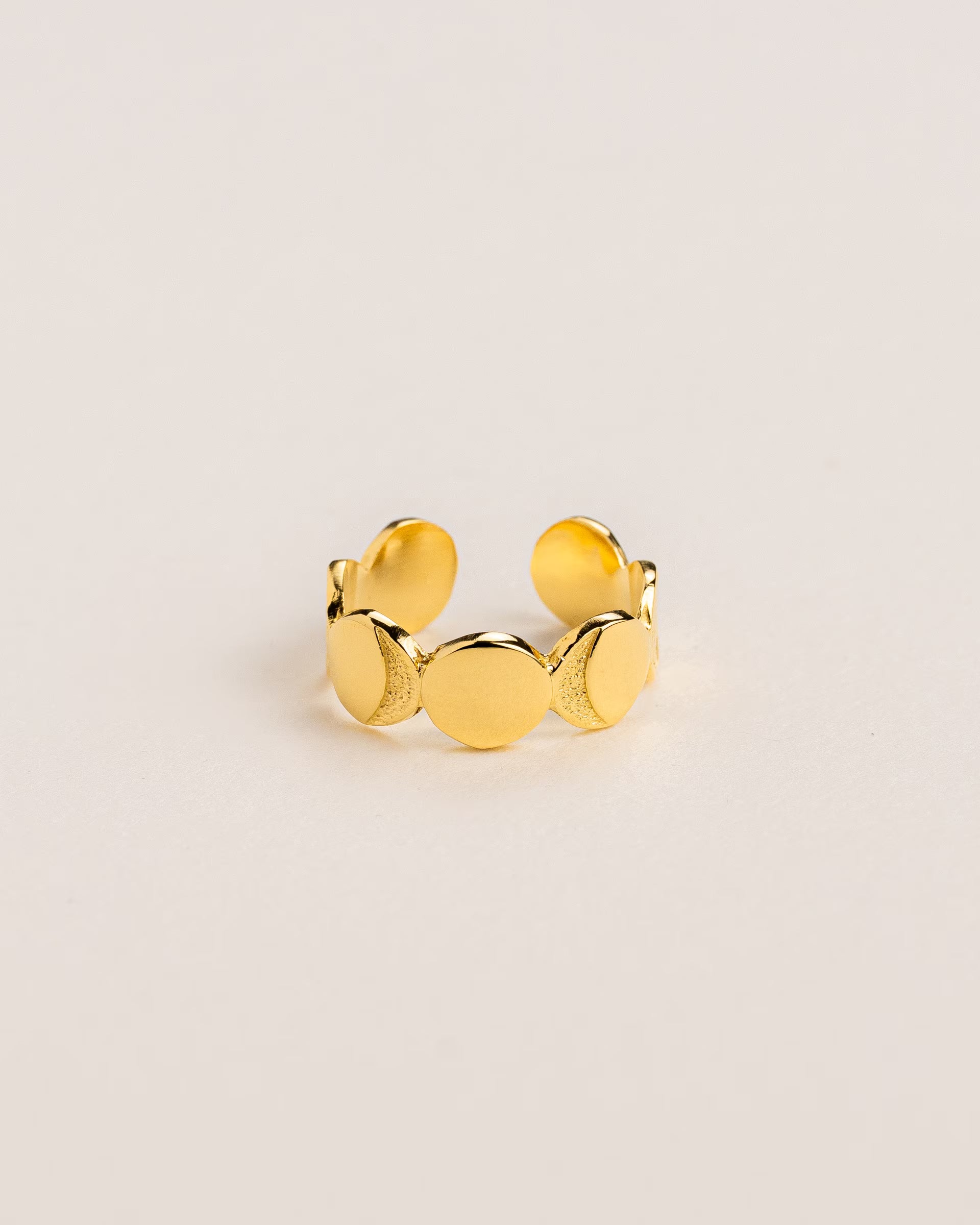 CHANDRA MOONPHASES RING GOLD, goldener Ring von ILUH, handgefertigt auf Bali – Elegantes Produktfoto im spirituellen Boho-Look von einem offenen, verstellbaren Ring aus 18k vergoldetem 925er Silber, der die verschiedenen Phasen des Mondes (Mondphasen) in einer durchgehenden, strukturierten Reihe zeigt, flach präsentiert auf einem hellen, neutralen Untergrund.