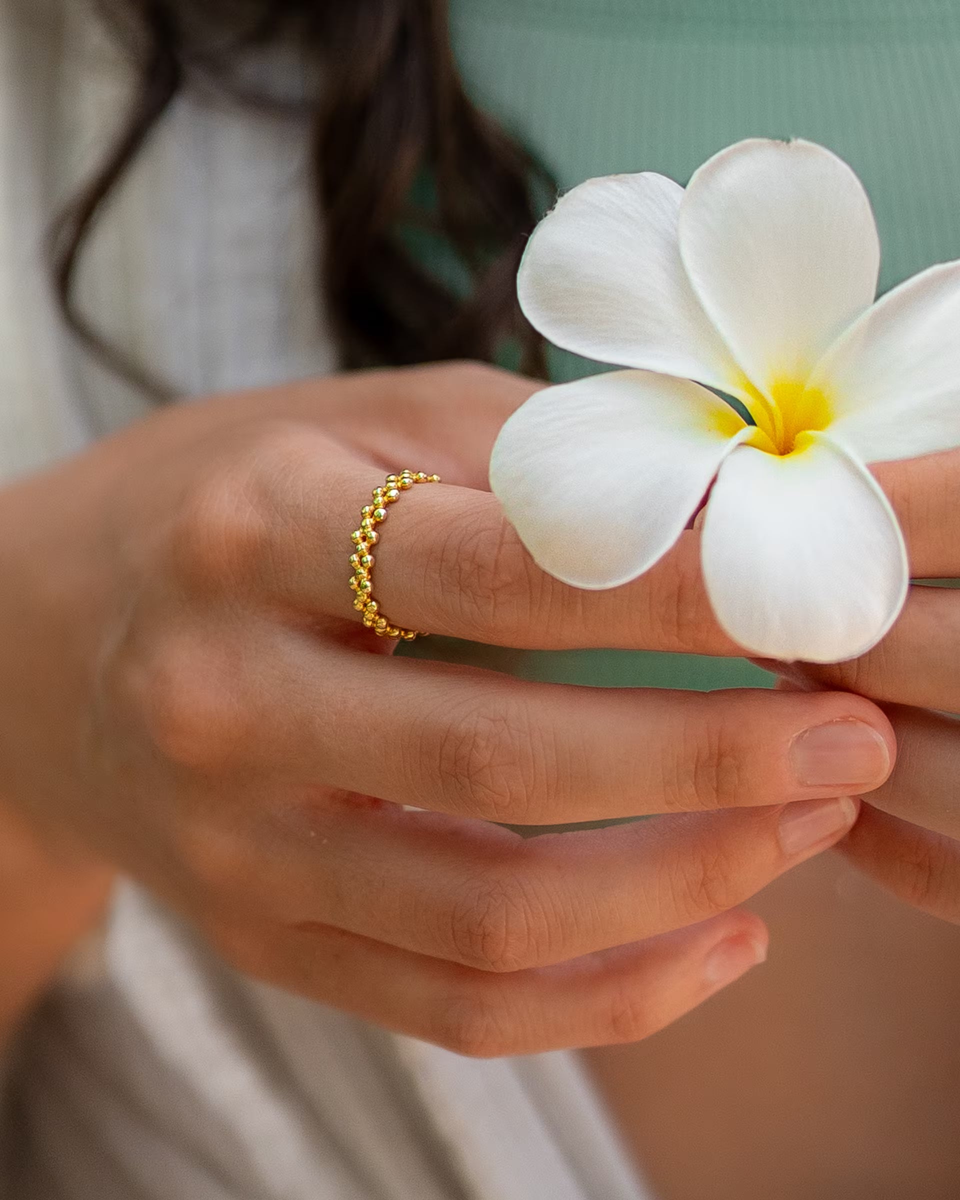 Handgefertigter ERIS Ring aus 18k vergoldetem 925er Silber von der Schmuckmarke ILUH, getragen an einer Hand von einer jungen Frau, die eine frische weiße Frangipani-Blüte hält.