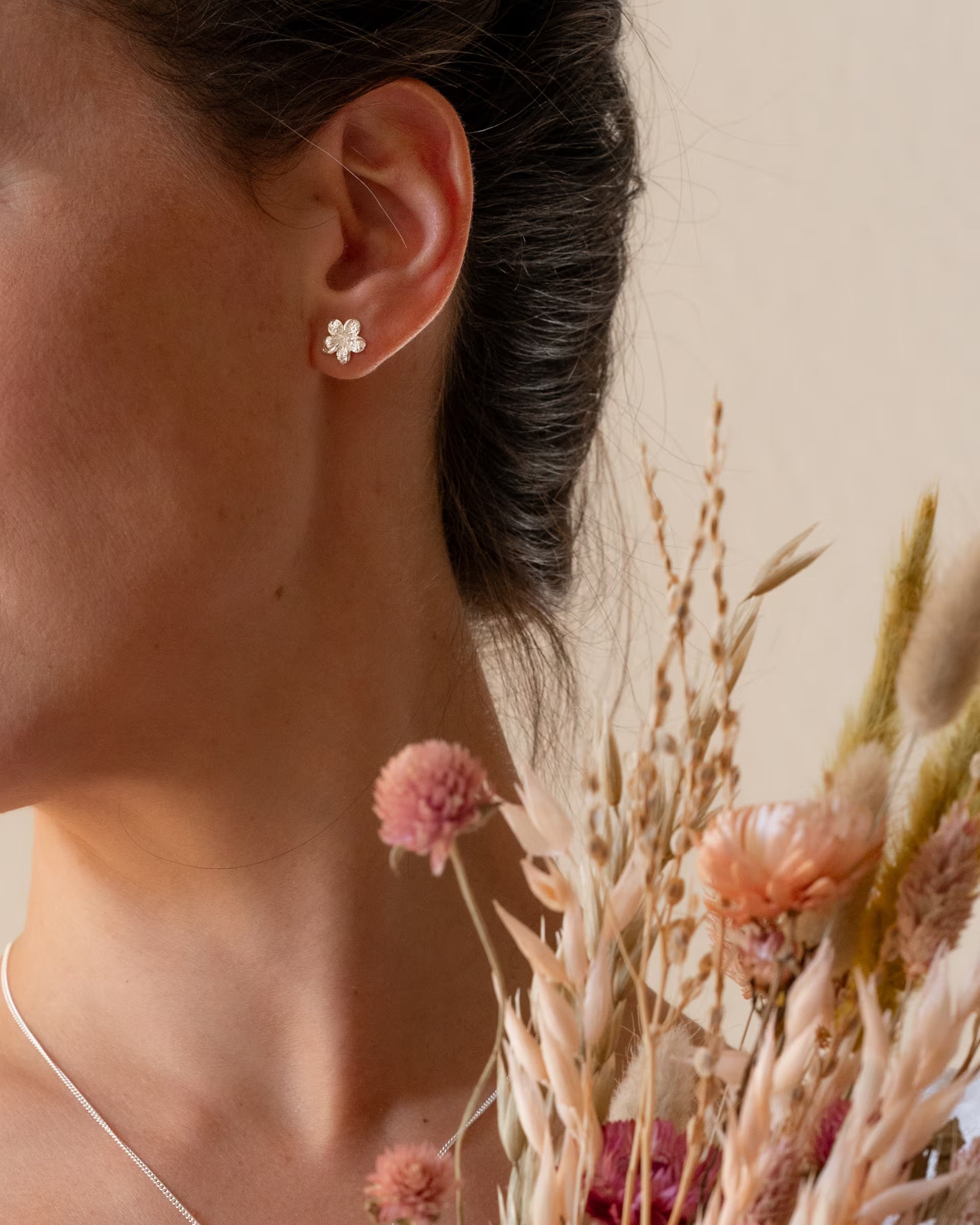 Nahaufnahme der handgefertigten Frangipani Ohrstecker aus 925er Silber von der Schmuckmarke ILUH, getragen im sanften Licht hinter einem Strauß aus Trockenblumen im verspielten Boho-Look.