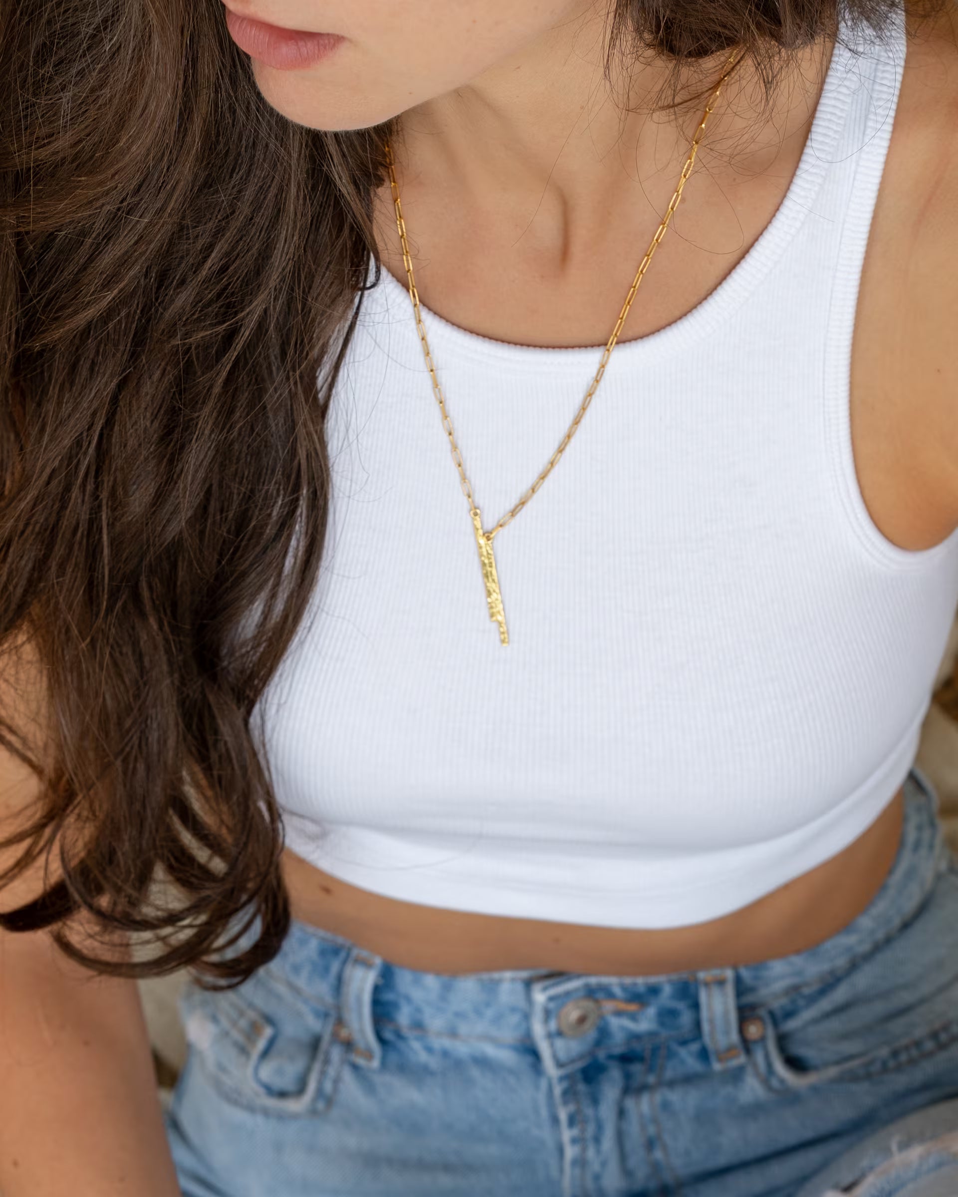 Junge Frau mit langen Haaren trägt die vergoldete FUSE Paperchain-Kette von der Schmuckmarke ILUH zu einem weißen Rippstrick-Crop-Top und Jeans.