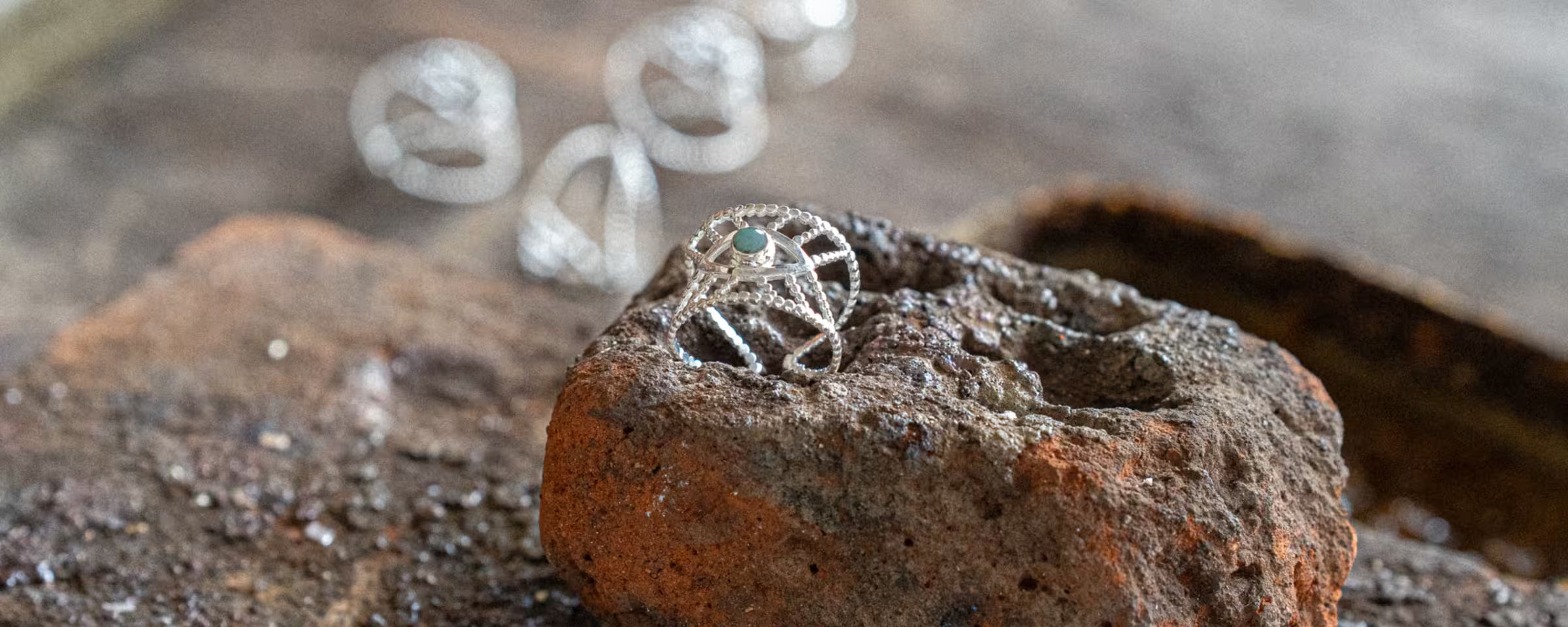 Detailreiche Produktaufnahme des handgefertigten 'Intuition'-Rings von ILUH, kunstvoll präsentiert auf einem rauen, rostigen Stein. Der filigrane Ring aus recyceltem 925 Sterling Silber mit einem grünen Smaragd Edelstein-Akzent steht für authentische balinesische Handwerkskunst und nachhaltige, spirituelle Eleganz. Dieses Bild unterstreicht den bewussten Lifestyle der Marke vor einem rustikalen, warm-erdigen Hintergrund.