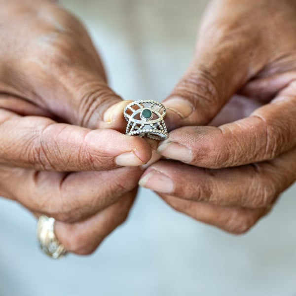 Detailaufnahme der Hände eines balinesischen Kunsthandwerkers, der einen filigranen ILUH Intuition-Ring aus 925 Silber mit Smaragd-Besatz hält. Das Bild verdeutlicht die faire Handarbeit und die hohe Schmuckqualität von ILUH Jewelry.