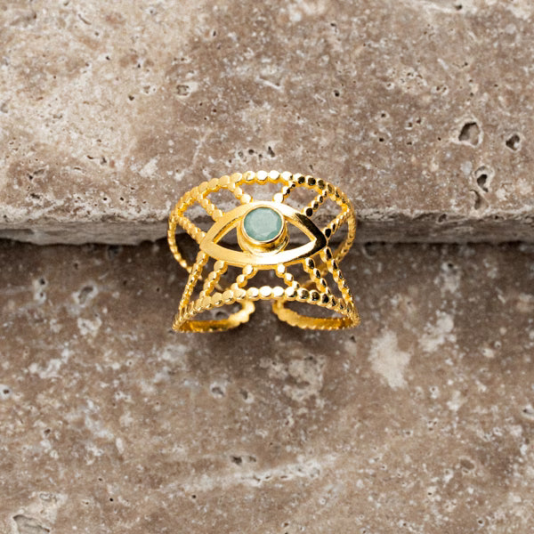 Studio-Nahaufnahme des Intuition-Rings in 18k Gold-Plating, präsentiert auf einer strukturierten, kühl-grauen Natursteinplatte. Der harte, marmorierte Untergrund bildet einen bewussten haptischen Kontrast zum warmen, glänzenden Gold des Rings und lässt die filigrane Struktur besonders leuchten. Der zentrale Smaragdstein fängt das Licht sanft ein und unterstreicht die feminine, moderne Ästhetik des Designs.