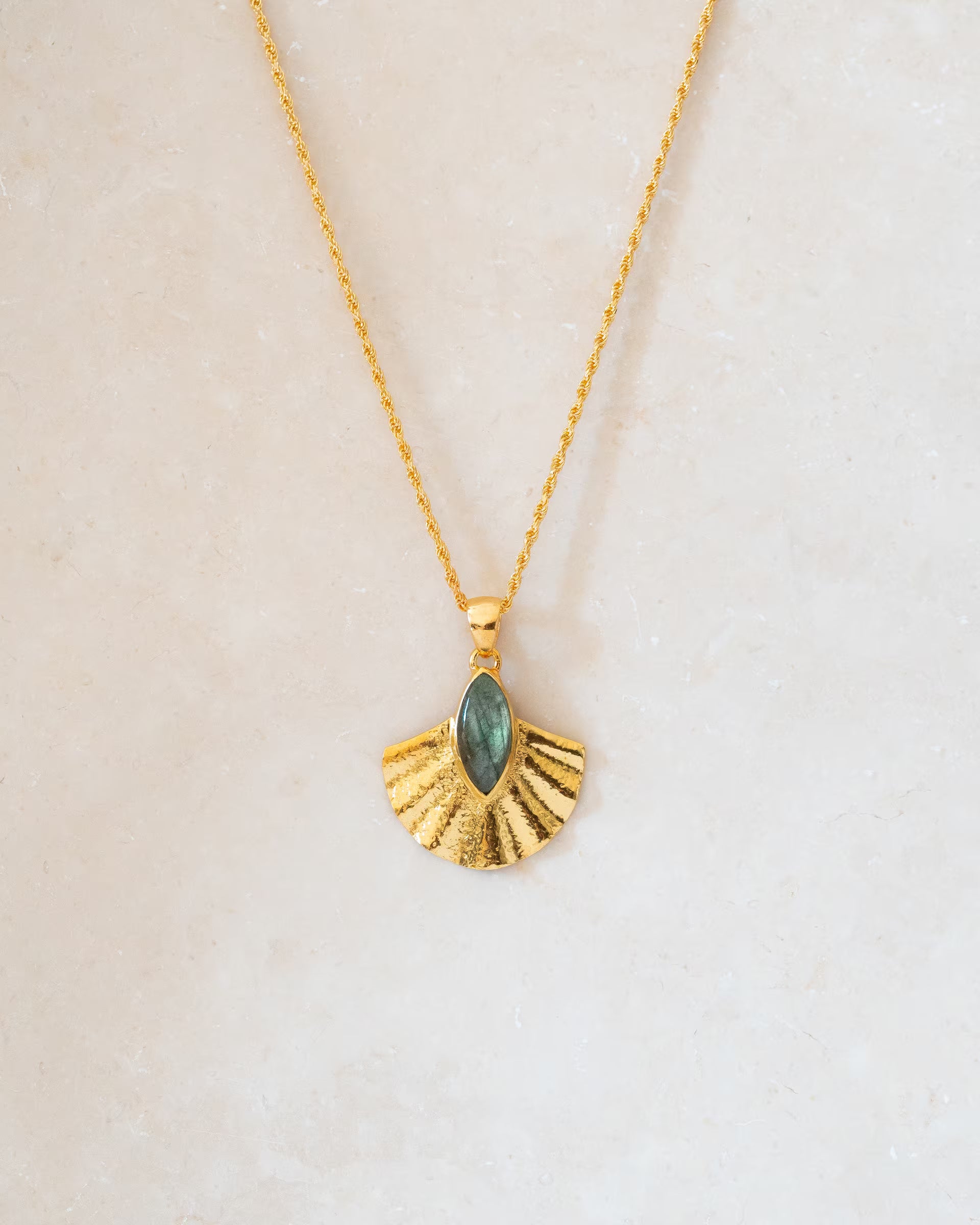 ALUN SHELL LABRADORITE HALSKETTE GOLD, goldene Halskette von ILUH, handgefertigt auf Bali – Stilvolles Produktfoto im minimalistischen Boho-Look von einer feinen Kette aus 18k vergoldetem 925er Silber mit einem fächerförmigen Anhänger, der eine reliefartige Struktur und einen mittig gefassten, marquise-förmigen Labradorit-Edelstein aufweist, flach präsentiert auf einem hellen Naturstein-Untergrund.