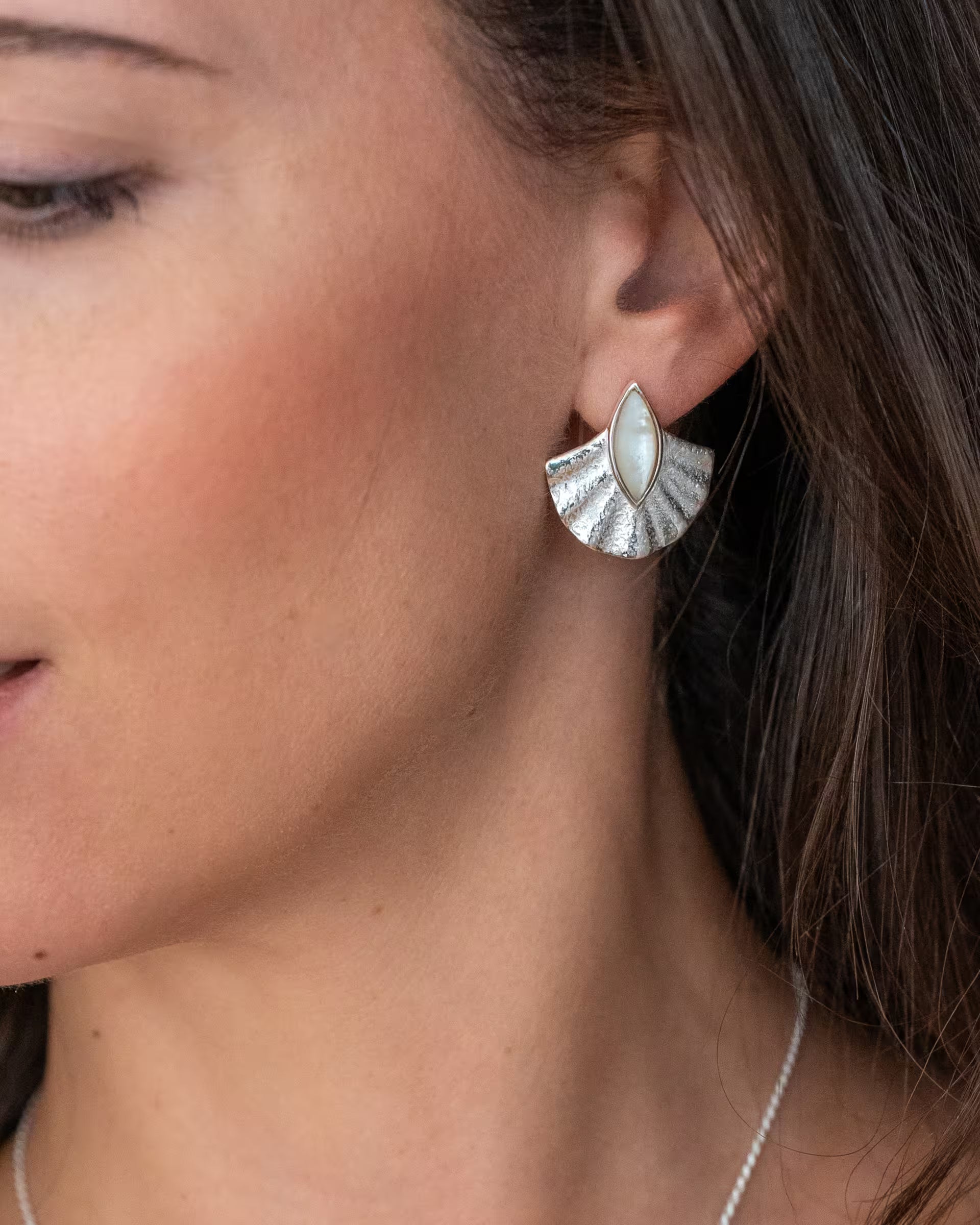 ALUN SHELL PERLMUTT OHRRINGE, silberner Boho-Schmuck von ILUH, handgefertigt auf Bali – Detailreiche Nahaufnahme im Profil von dem Ohr einer Frau mit langen braunen Haaren, die das fächerförmige Muschel-Design aus 925er Silber mit edel schimmerndem, weißem Perlmutt elegant präsentiert.