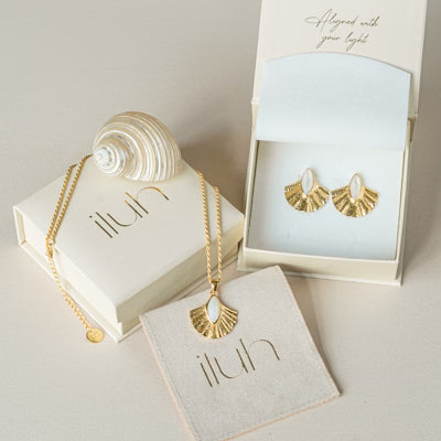 Luxuriöses ILUH Schmuck-Set in cremefarbener, nachhaltiger Geschenkverpackung; abgebildet sind Ohrringe und eine Kette aus der ALUN-Kollektion (Präsentationsbeispiel) in Kombination mit einer natürlichen Muschel für ein ästhetisches, handgefertigtes Unboxing-Erlebnis.