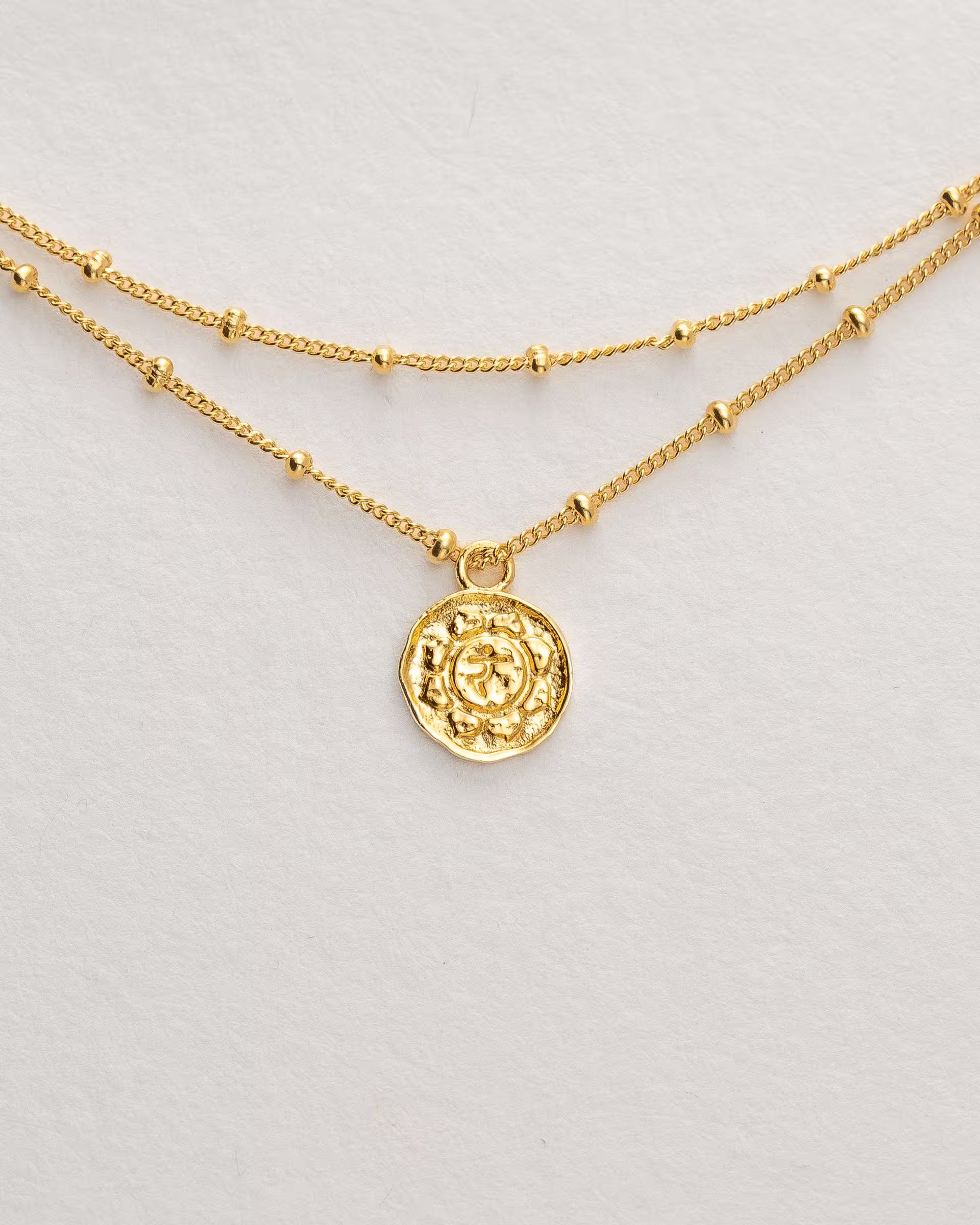 Filigranes ILUH Armband aus 18k vergoldetem, recyceltem Silber mit doppellagiger Kette und einem runden Anhänger mit Herz-Chakra-Motiv; Nahaufnahme auf strukturiertem Büttenpapier, die das zarte Design und die hochwertige Handwerkskunst hervorhebt – ein zeitloses Schmuckstück, das Liebe, Harmonie und Mitgefühl symbolisiert.