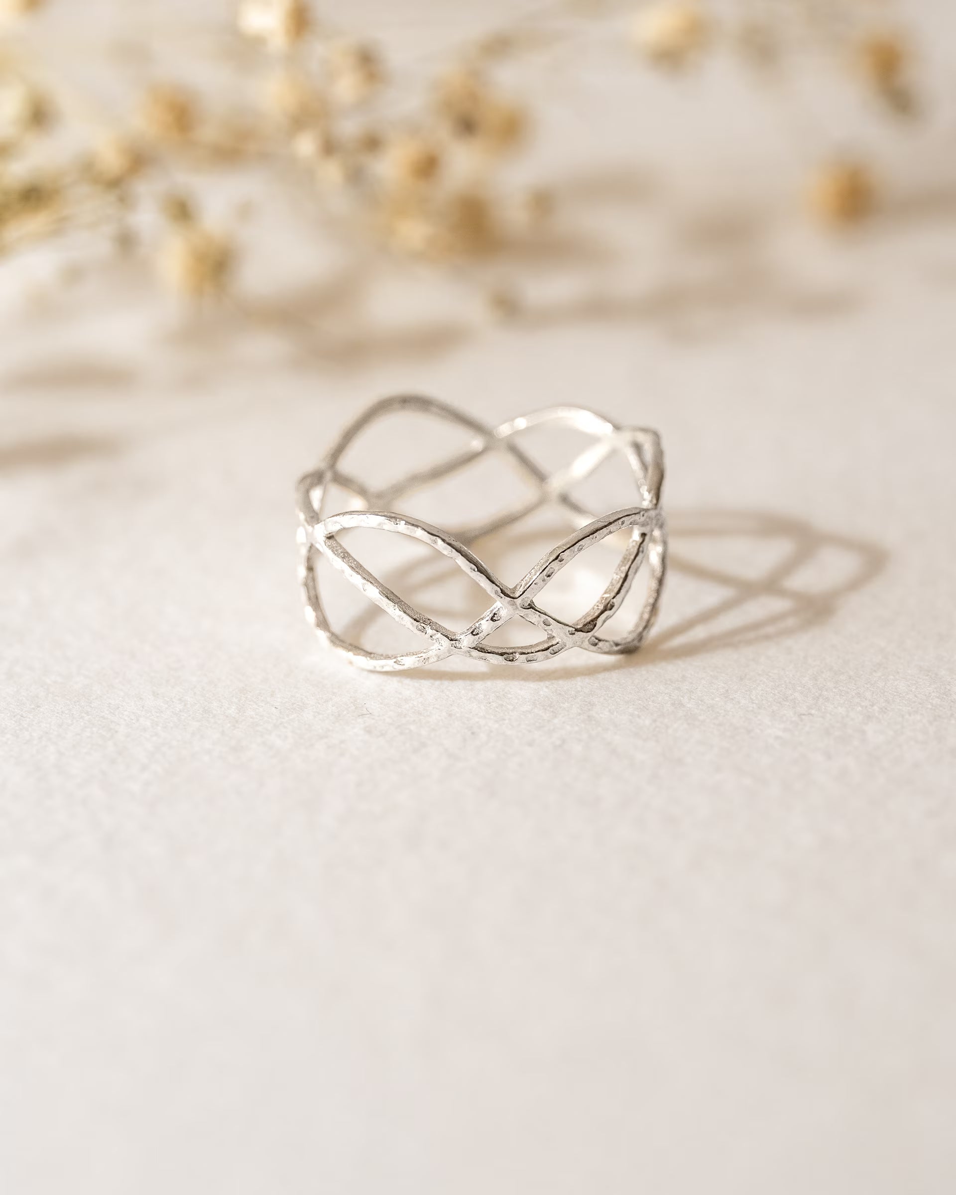 Produktbild „Lotus Ring Silber”- 
Dieser handgefertigte Ring von ILUH aus Bali im minimalistischen Boho-Stil besticht durch sein filigranes Lotusblüten-Design mit einer fein gehämmerten Struktur. Die Lotusblüte gilt als Symbol für Reinheit und spirituelles Erwachen. Sie ist kunstvoll auf einem hellen Büttenpapier platziert und wird von Trockenblüten im Hintergrund umrahmt.
