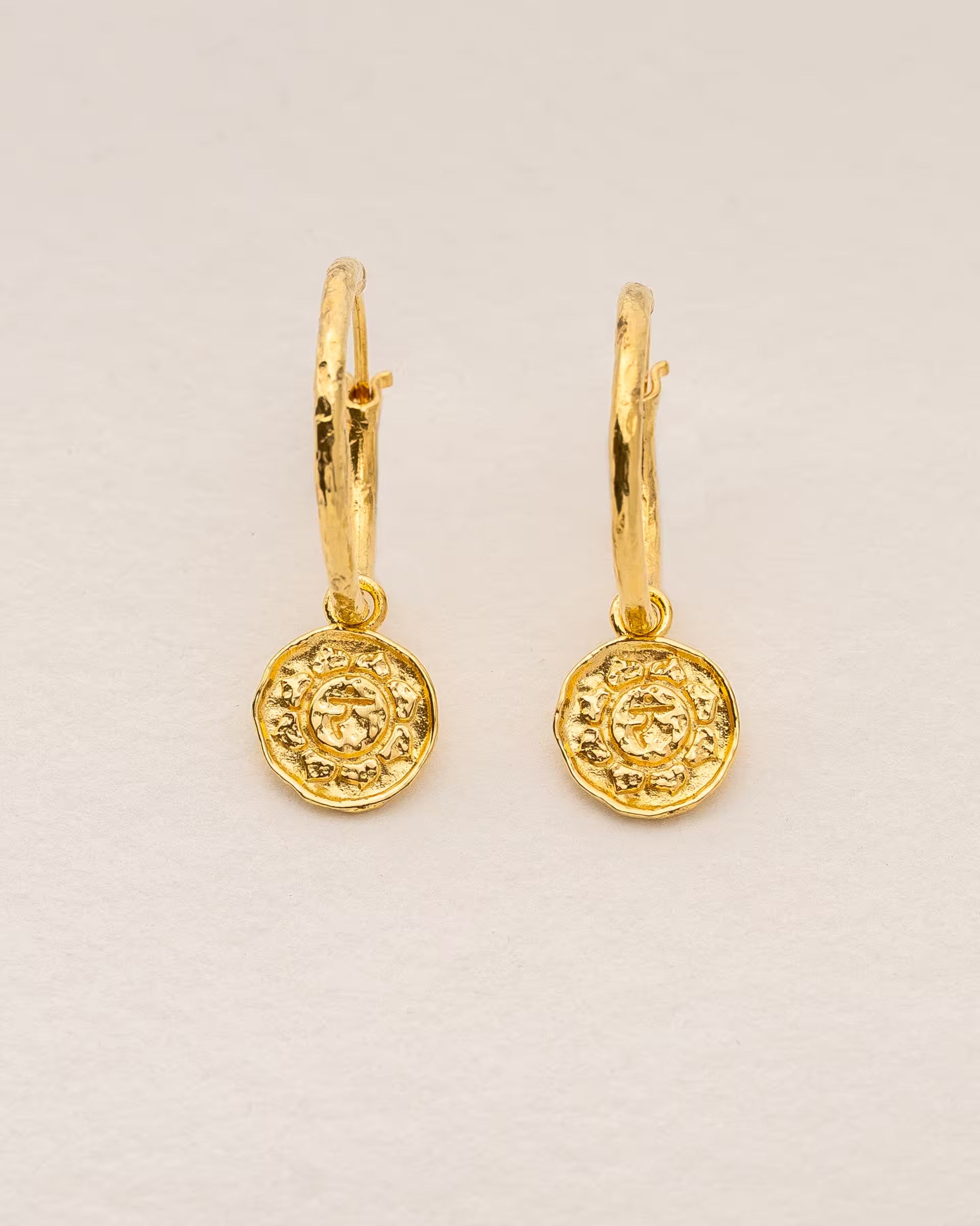 #Motiv_Manipura CHAKRA MANIPURA OHRRINGE GOLD Produktbild – Diese handgefertigten Ohrringe von ILUH aus Bali im minimalistischen Stil bestehen aus strukturierten Creolen mit einem runden Anhänger, der das originale Sanskrit-Zeichen für das Manipura-Solarplexuschakra zeigt; eingebettet in kunstvolle Lotusblütenblätter dienen sie als kraftvolles Symbol zur Stärkung deines Energiezentrums.