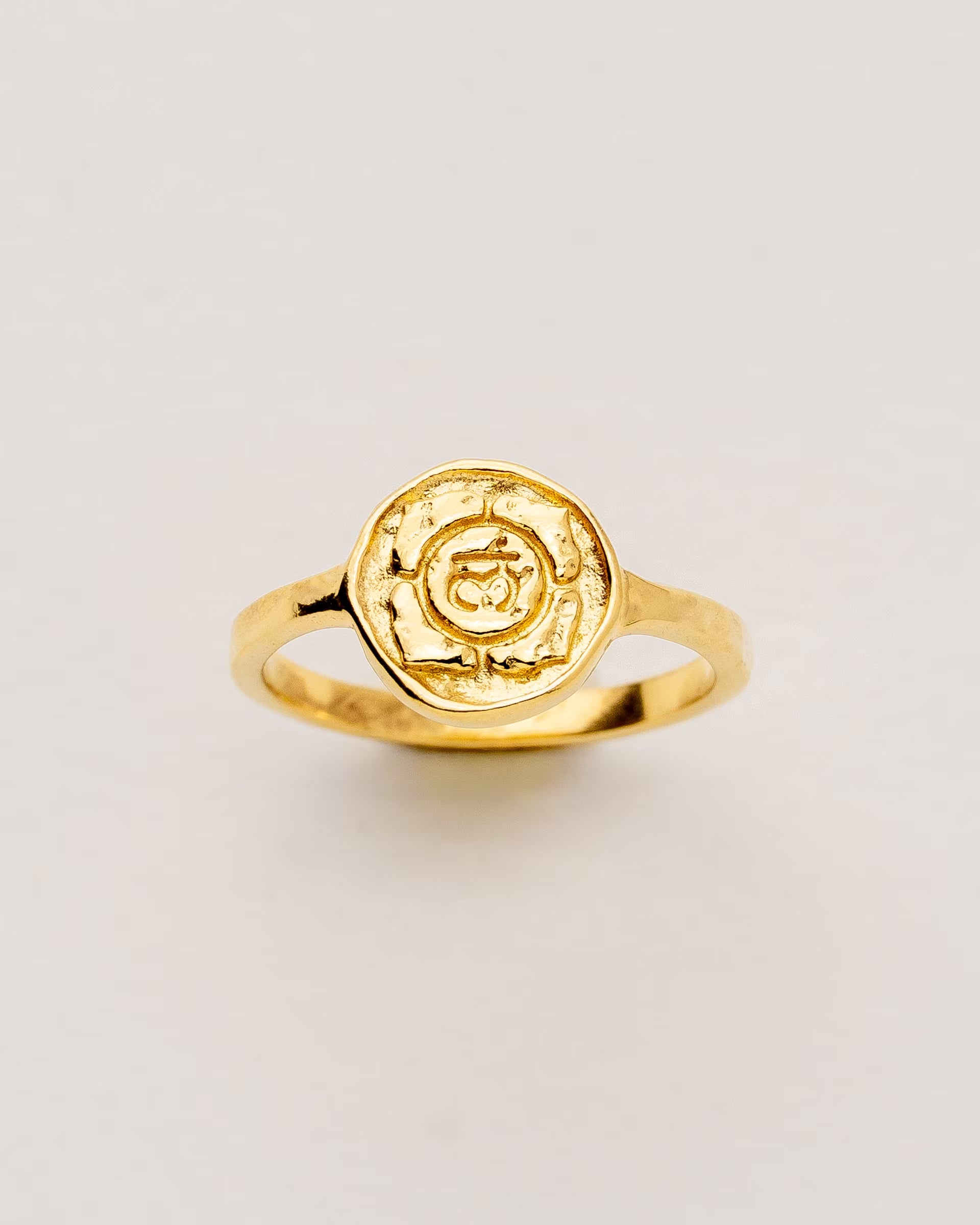 #Motiv_Muladhara CHAKRA MULADHARA RING GOLD – Dieser handgefertigte Siegelring von ILUH aus Bali im minimalistischen Stil überzeugt durch eine runde, strukturierte Platte, die das originale Sanskrit-Zeichen für das Muladhara-Wurzelchakra zeigt; eingebettet in kunstvolle Lotusblütenblätter dient er als kraftvolles Symbol zur Stärkung deines Energiezentrums.