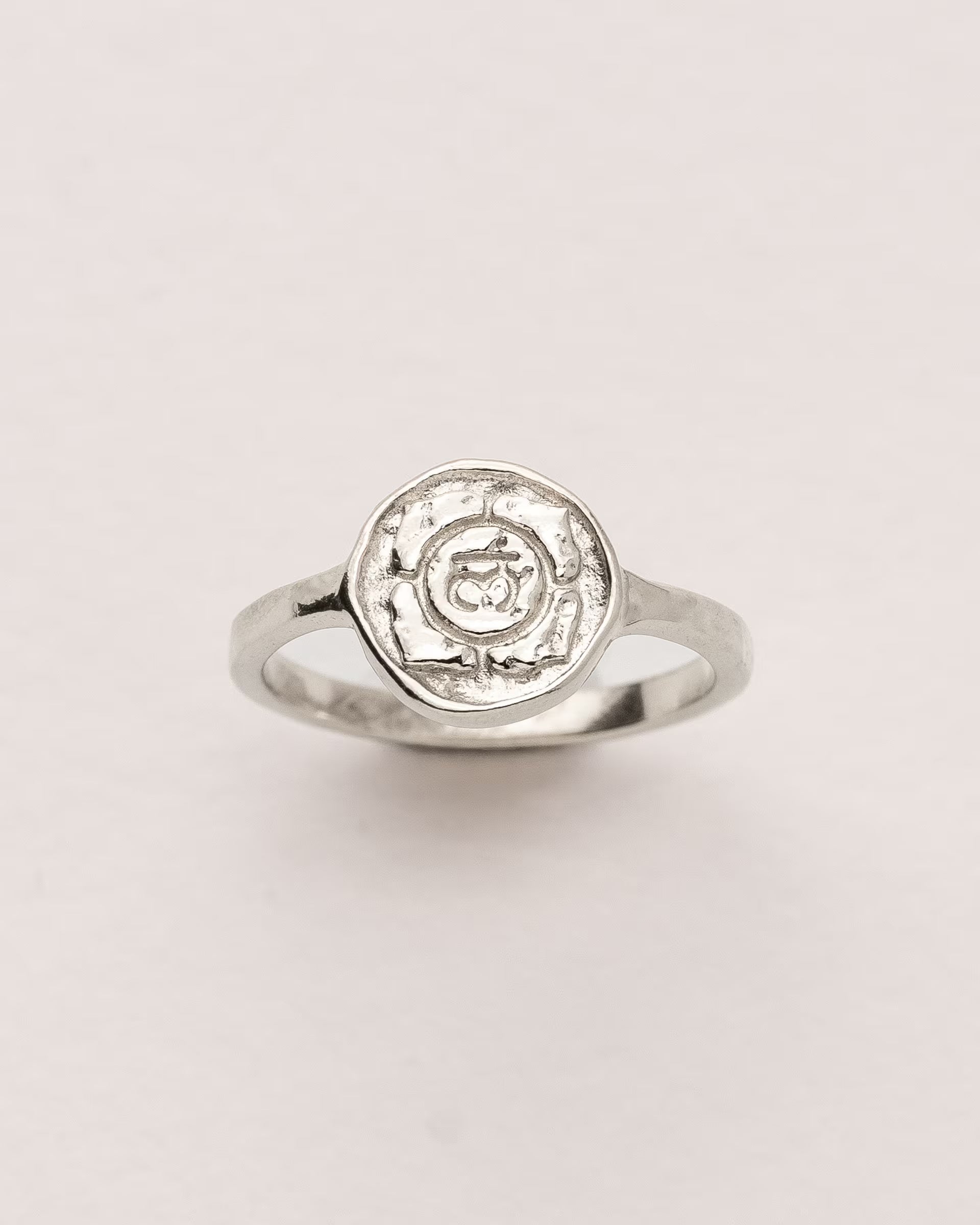 #Motiv_Muladhara CHAKRA MULADHARA RING SILBER, silberner Siegelring von ILUH, handgefertigt auf Bali – Spirituelles Produktfoto im minimalistischen Look von einem Siegelring mit einer runden, strukturierten Platte, die das originale Sanskrit-Zeichen für das Muladhara-Wurzelchakra, eingebettet in kunstvolle Lotusblütenblätter zur Stärkung des Energiezentrums, zeigt.