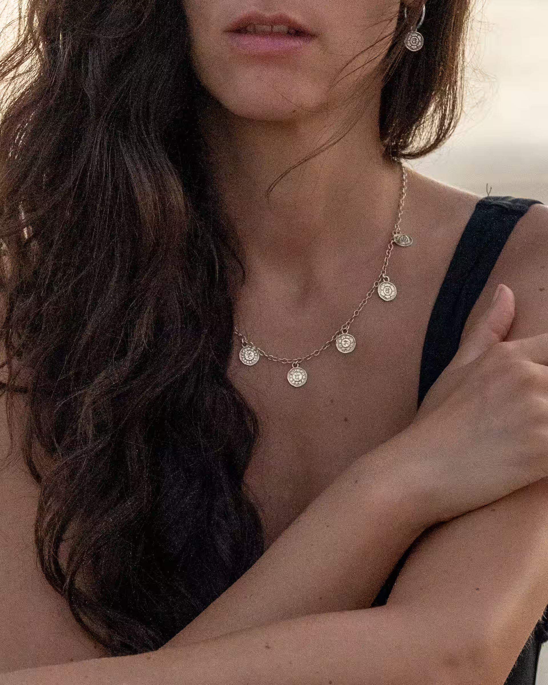 Handgefertigte PRANA Halskette aus 925er Silber mit den 7 Chakren-Motiven und Chakra Creolen-Ohrringe vom JEWELRY LABEL ILUH, getragen von einer jungen Frau im eleganten Sommer-Look am Strand als detailreiche Nahaufnahme.
