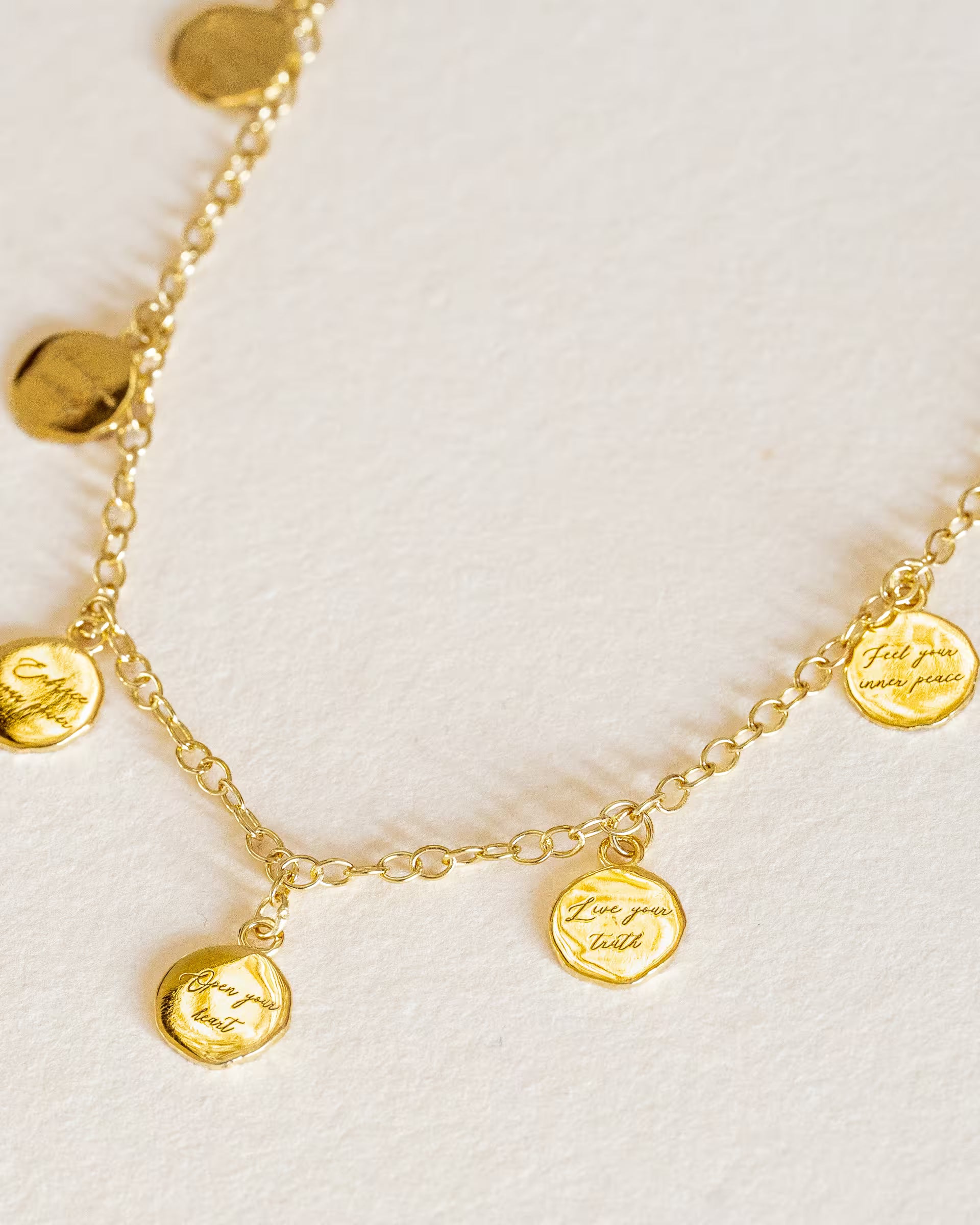 Goldene Halskette von ILUH mit feinen, gravierten Medaillons; das Design kombiniert minimalistischen Schmuck-Stil mit spirituellen Botschaften aus der Chakra-Philosophie, präsentiert in einer hochwertigen Makro-Aufnahme.
