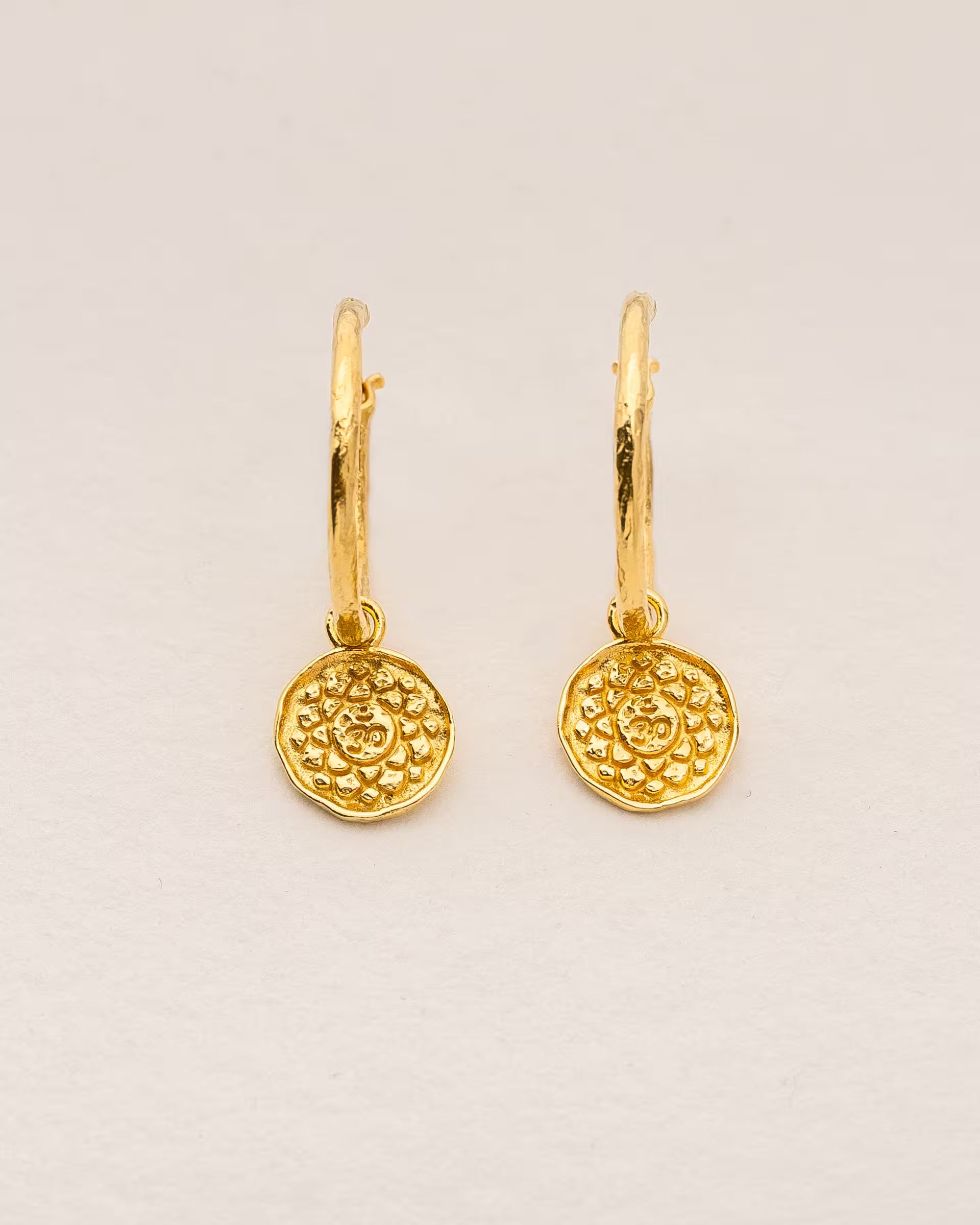 #Motiv_Sahasrara CHAKRA SAHASRARA OHRRINGE GOLD Produktbild – Diese handgefertigten Ohrringe von ILUH aus Bali im minimalistischen Boho-Stil bestehen aus strukturierten Creolen mit einem runden Anhänger, der das originale Sanskrit-Zeichen für das Sahasrara-Kronenchakra zeigt; eingebettet in kunstvolle Lotusblütenblätter dienen sie als kraftvolles Symbol zur Stärkung deines Energiezentrums.