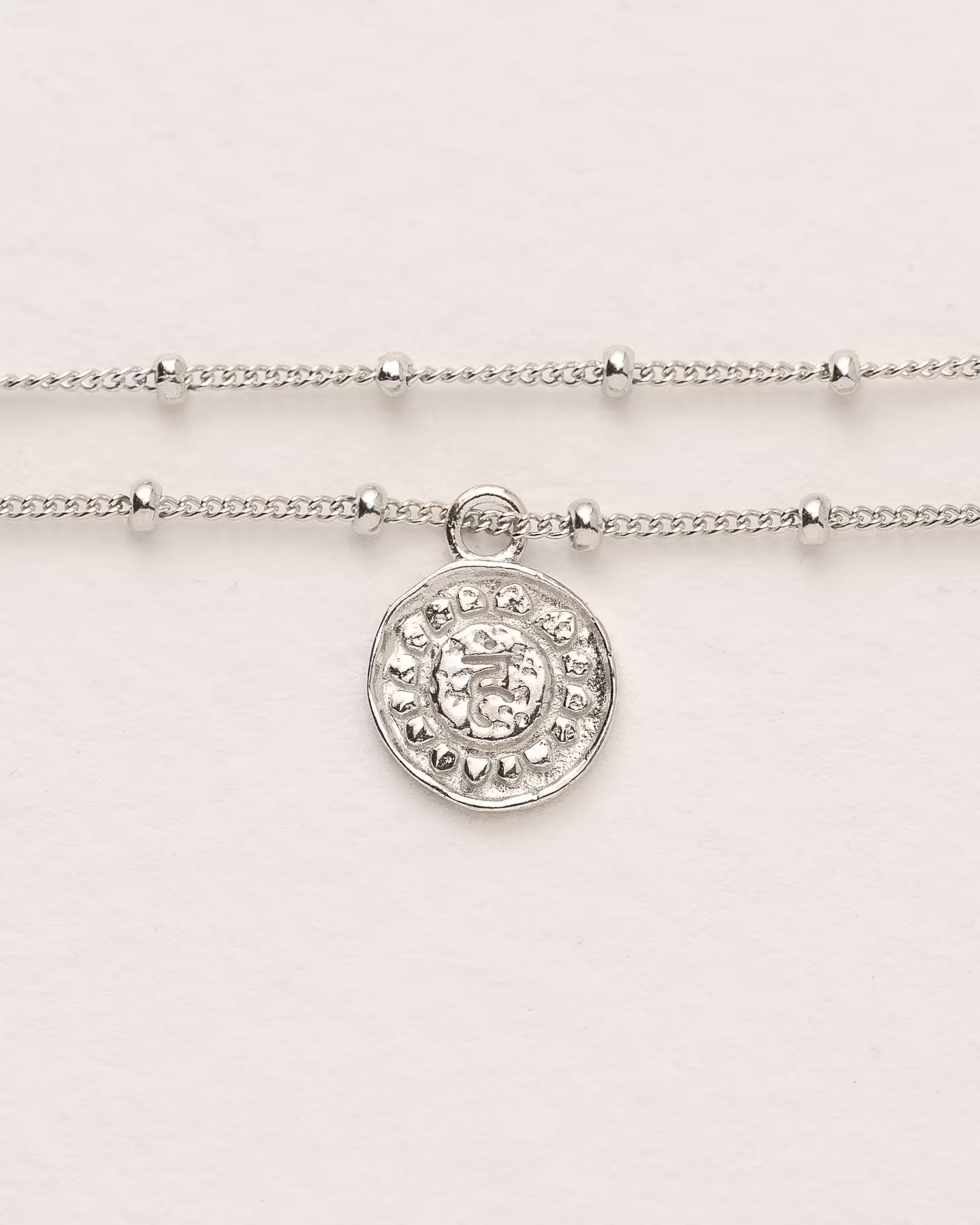 #Motiv_Vishuddha CHAKRA VISHUDDHA ARMBAND SILBER Produktbild – Dieses handgefertigte, silberne Armband mit einer feinen, doppelten Satellitenkette von der Schmuckmarke ILUH aus Bali im minimalistischen Stil zeigt das originale Sanskrit-Zeichen für das Vishuddha-Halschakra; eingebettet in kunstvolle Lotusblütenblätter dient es als kraftvolles Symbol zur Stärkung deines Energiezentrums.