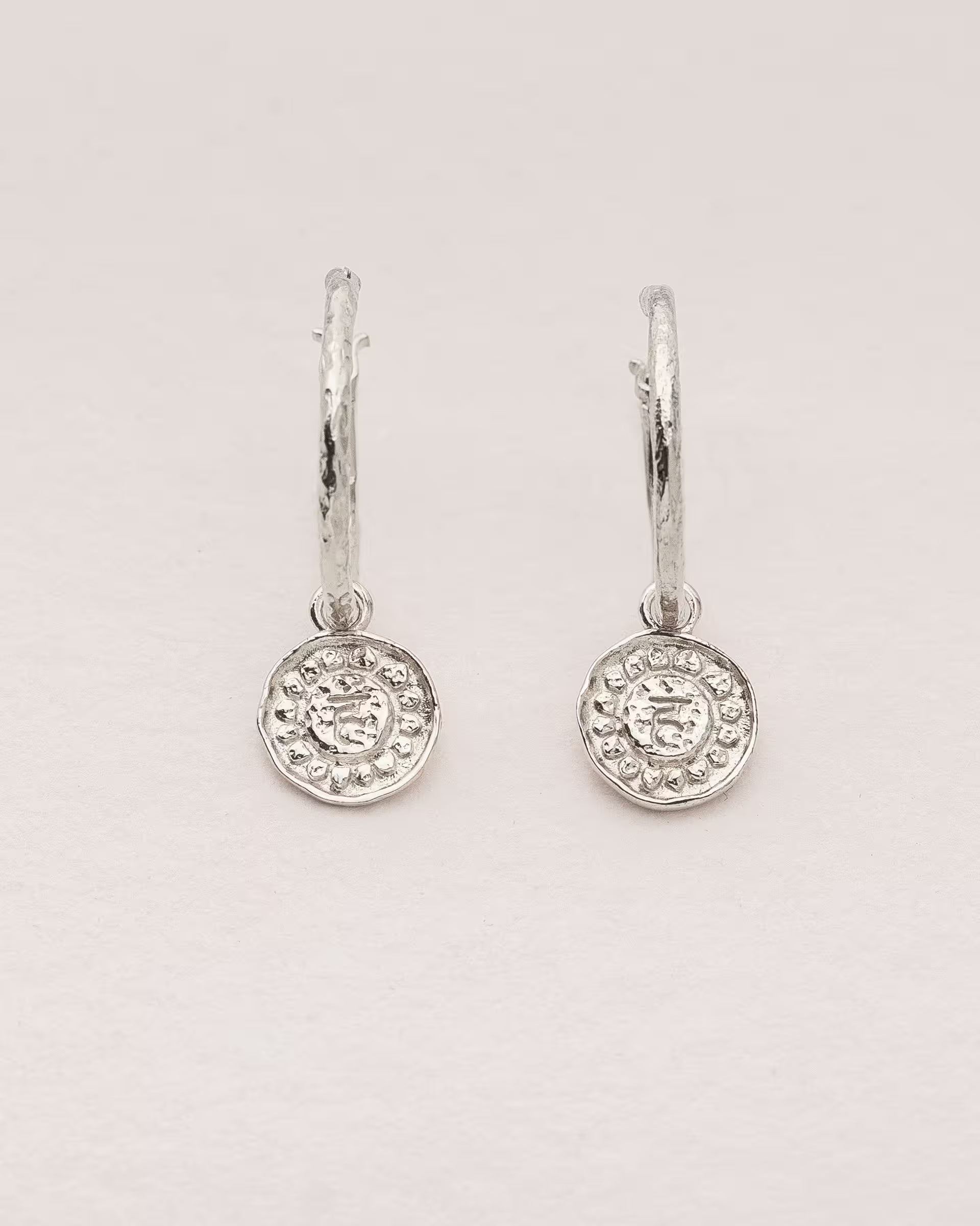 #Motiv_Vishuddha CHAKRA VISHUDDHA OHRRINGE SILBER Produktbild – Diese handgefertigten Ohrringe von ILUH aus Bali im minimalistischen Boho-Stil bestehen aus strukturierten Creolen mit einem runden Anhänger, der das originale Sanskrit-Zeichen für das Vishuddha-Halschakra zeigt; eingebettet in kunstvolle Lotusblütenblätter dienen sie als kraftvolles Symbol zur Stärkung deines Energiezentrums.