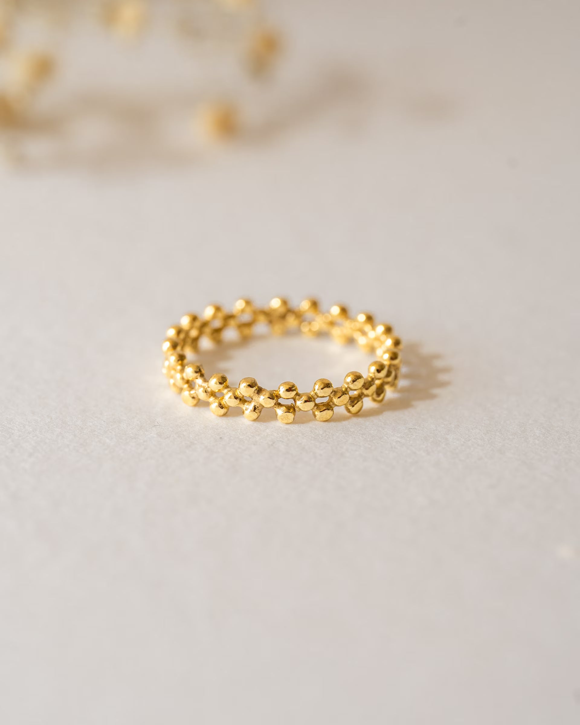 ERIS RING GOLD Produktbild – Diese zarte Nahaufnahme zeigt den goldenen Eris-Ring von ILUH im cleanen Design; das Schmuckstück besticht durch seine filigrane, perlenartige Struktur, die aneinandergereihte kleine Kügelchen kunstvoll miteinander verbindet.