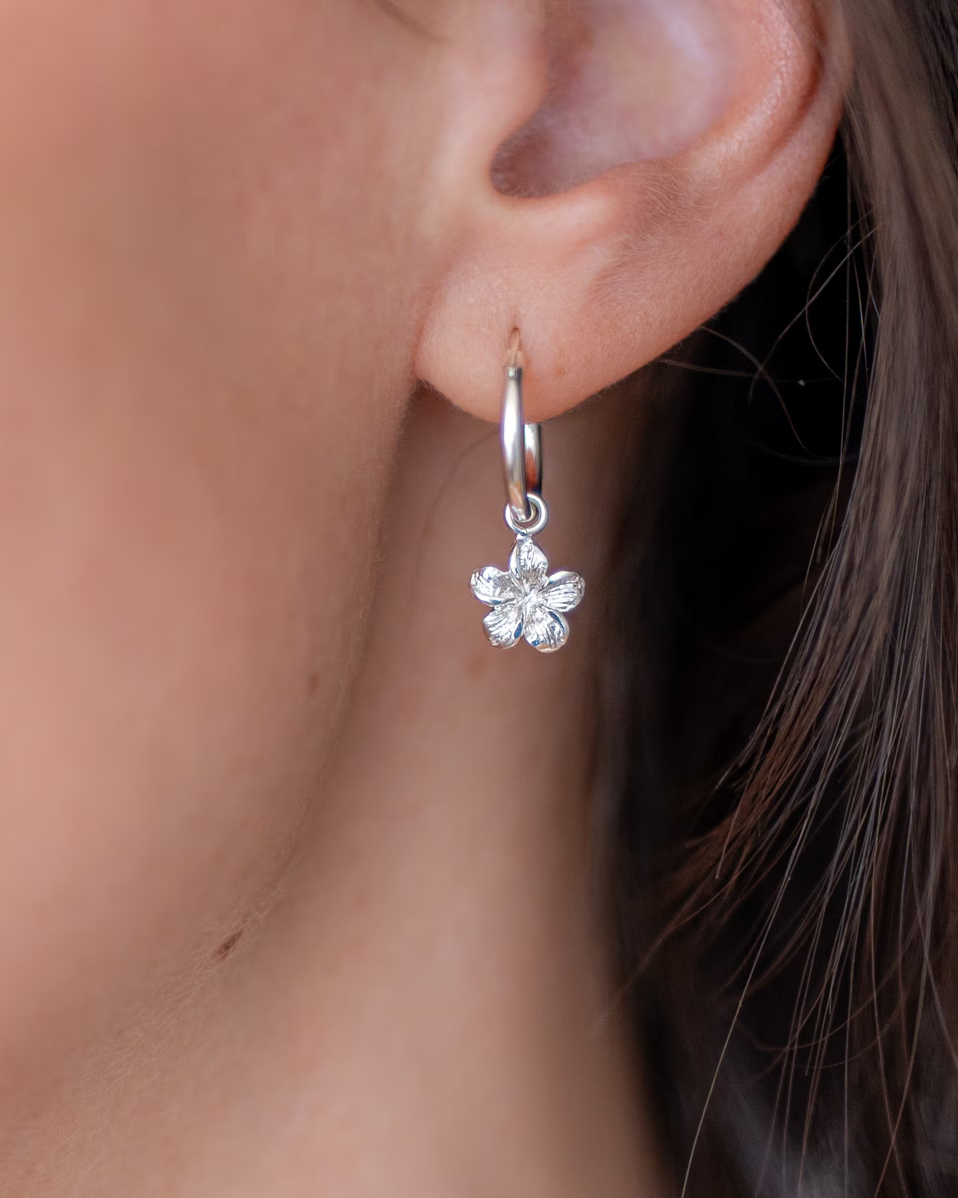 Nahaufnahme der handgefertigten silbernen Creolen mit einer tropischen Frangipani-Blüte aus der Kollektion vom Schmucklabel ILUH für den perfekten Sommer-Look.