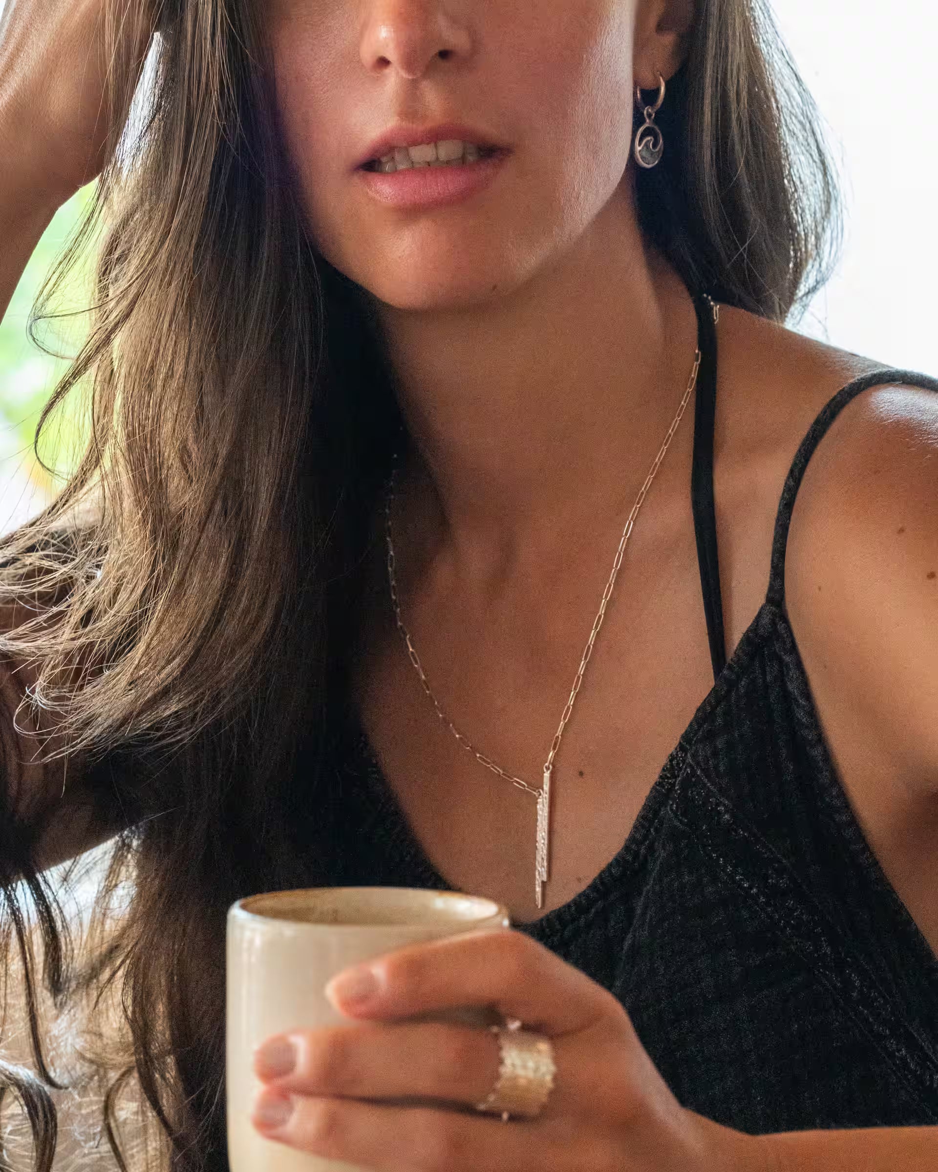 Junge Frau im Café mit der filigranen FUSE Silberkette und den LAJU Silberohrringen des Schmuck-Labels ILUH.
