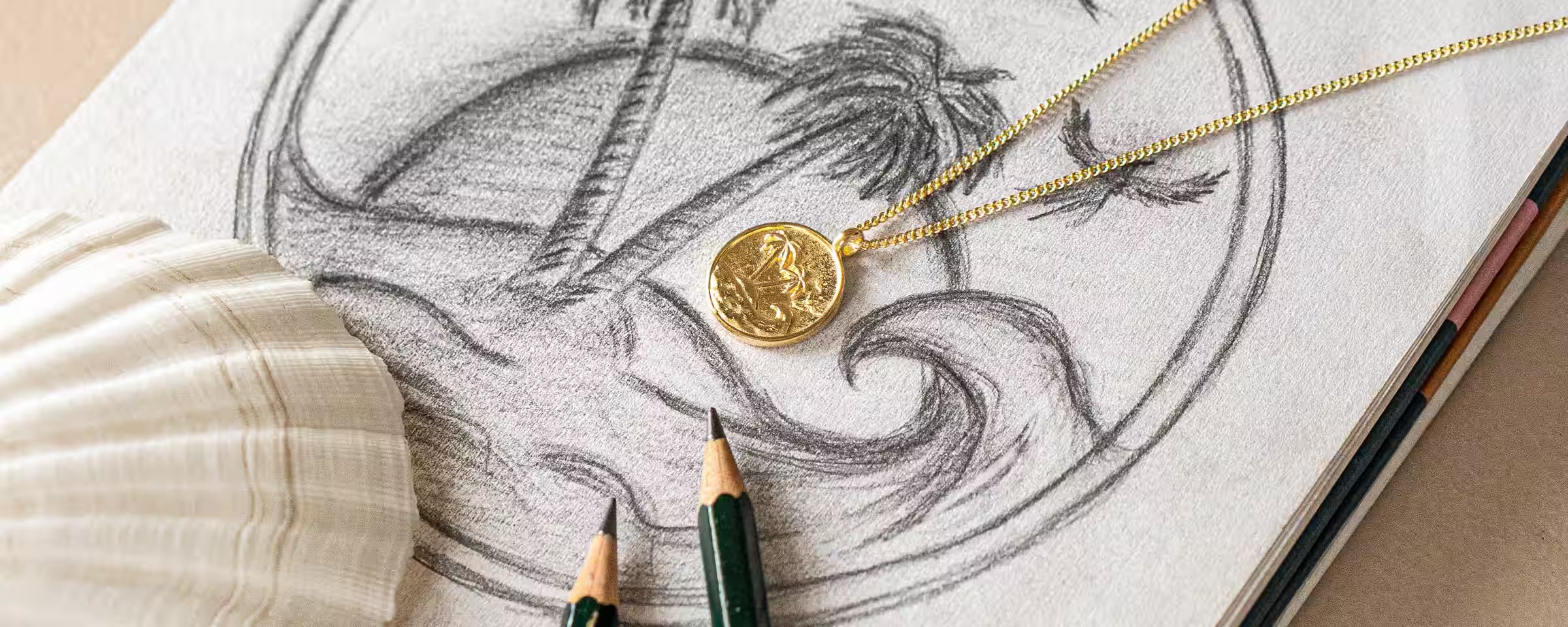 Künstlerische Nahaufnahme der Inspiration hinter ILUH Jewelry: Eine detaillierte Skizze eines Insel-Motivs mit Palmen und Wellen neben einer filigranen, 18k vergoldeten Halskette. Ein Symbol für die handwerkliche Qualität und den kreativen Designprozess unseres Schmucks aus Bali.