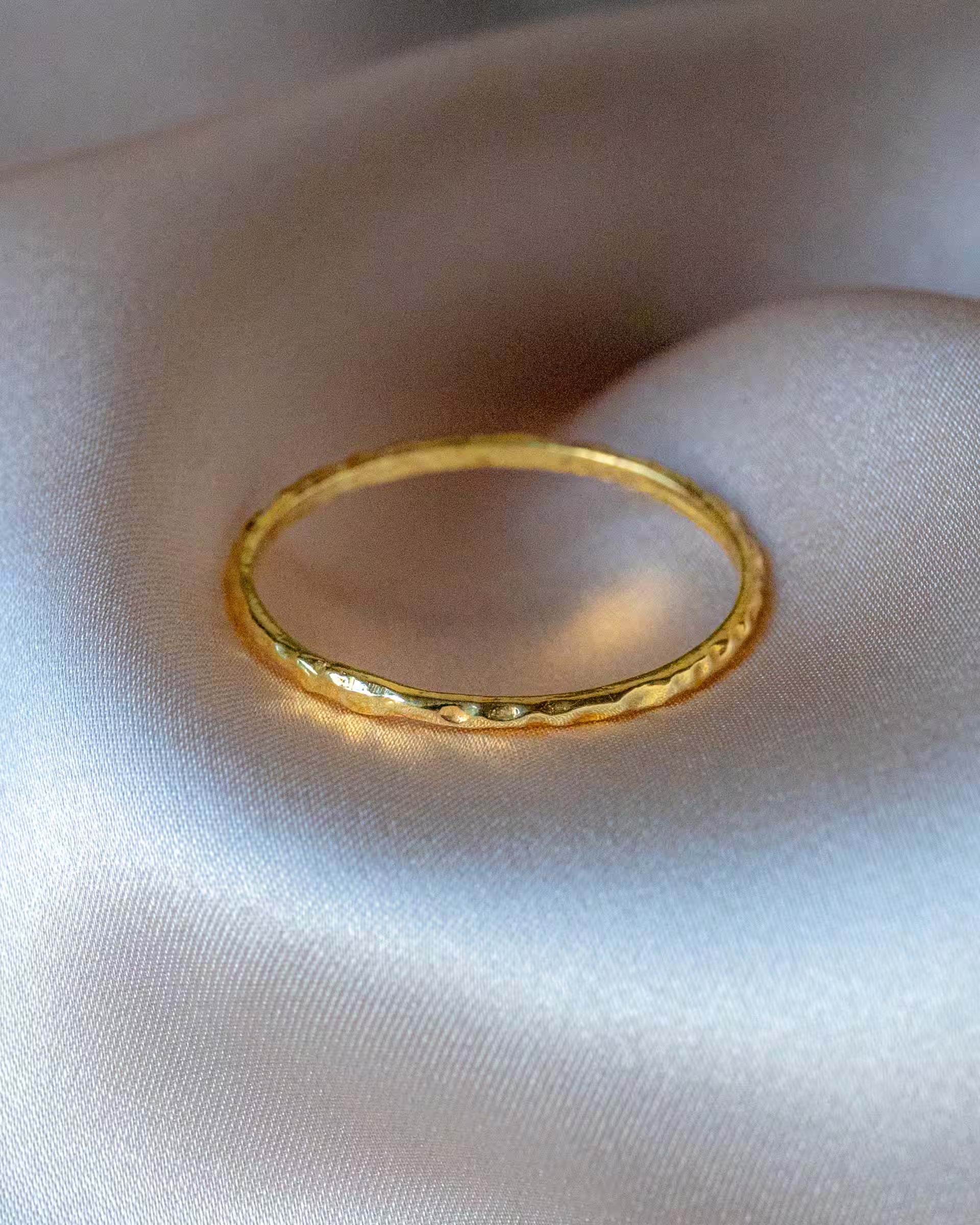 Auf Bali handgefertigter goldener SARI Ring mit gehämmerter, strukturierter Oberfläche aus 18k vergoldetem 925er Silber von der Schmuckmarke ILUH, als Produktfoto platziert auf glänzender, cremefarbener Seide.