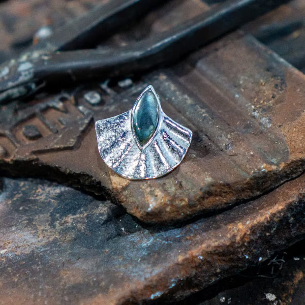 Detailaufnahme eines silbernen Alun-Ohrrings von ILUH mit Labradorit Edelstein, präsentiert auf einem rustikalen, dunklen Stein. Das Bild betont die Handwerkskunst des fair in Bali gefertigten Schmuckstücks aus 925 Sterling Silber und hebt die organische Textur sowie die spirituelle Note der Marke ILUH hervor.