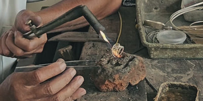 Ein erfahrener Silberschmied fertigt in einer friedvollen, sonnendurchfluteten Werkstatt auf Bali einen ILUH Intuition-Ring; das warme Licht und die ruhigen, präzisen Handbewegungen beim Löten unterstreichen die meditative und achtsame Handarbeit hinter jedem Schmuckstück.