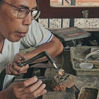 Ein erfahrener Silberschmied fertigt in einer friedvollen, sonnendurchfluteten Werkstatt auf Bali einen ILUH Intuition-Ring; das warme Licht und die ruhigen, präzisen Handbewegungen beim Löten unterstreichen die meditative und achtsame Handarbeit hinter jedem Schmuckstück.